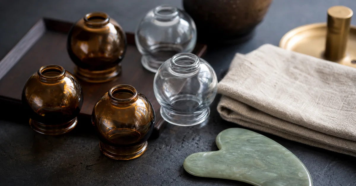 Schröpfgläser und ein Gua-Sha-Schaber nebeneinander auf einem Tuch